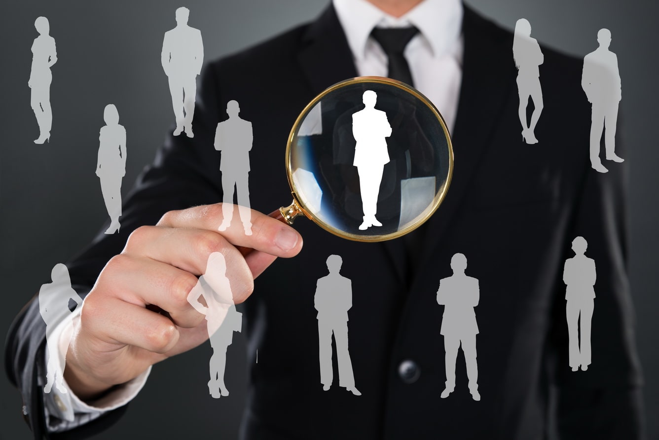 midsection-of-businessman-searching-candidate-with-magnifying-glass-over-gray-background